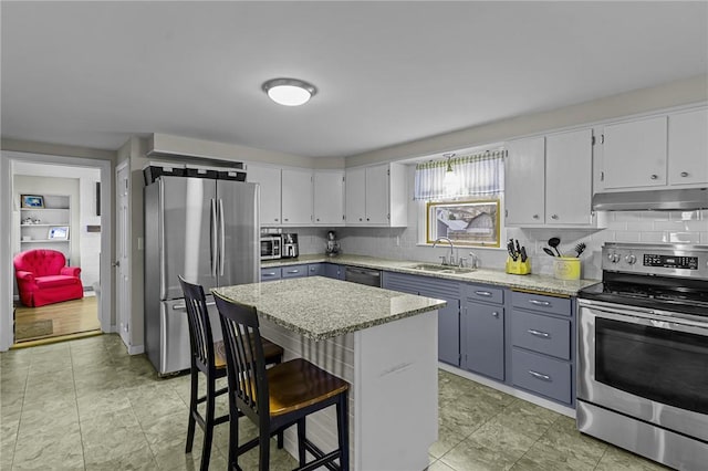 kitchen featuring a center island, sink, light stone countertops, appliances with stainless steel finishes, and a breakfast bar area