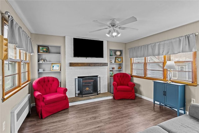 living room featuring a brick fireplace, ceiling fan, dark hardwood / wood-style floors, built in shelves, and radiator heating unit