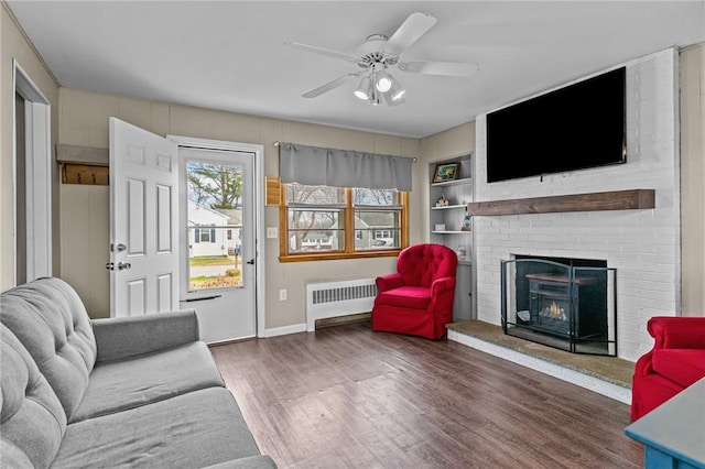 living room with dark wood-type flooring, radiator, ceiling fan, built in features, and a fireplace