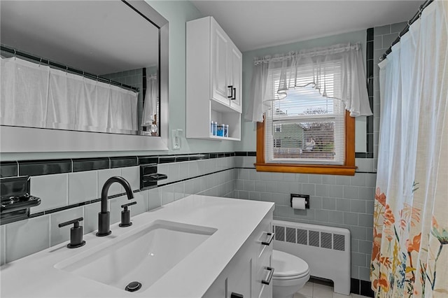 bathroom with vanity, backsplash, radiator, toilet, and tile walls