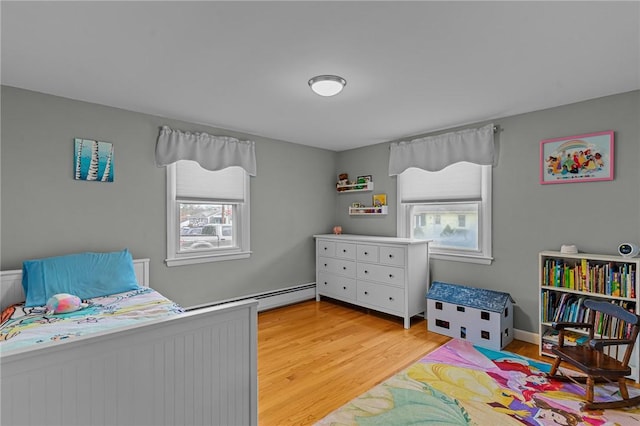 bedroom featuring light hardwood / wood-style floors, multiple windows, and a baseboard heating unit