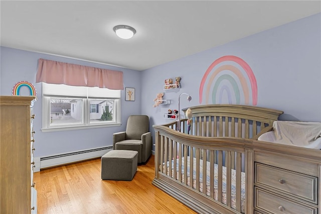 bedroom with a nursery area, light wood-type flooring, and a baseboard heating unit