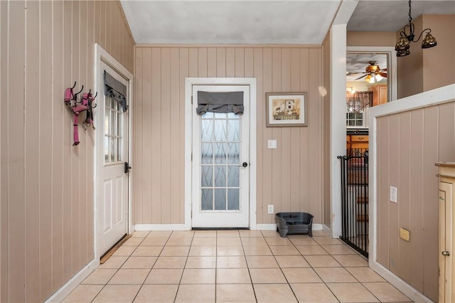 doorway with light tile patterned floors, ceiling fan with notable chandelier, and wooden walls