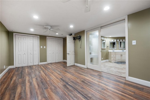 unfurnished bedroom featuring ceiling fan, wood-type flooring, ensuite bathroom, and multiple closets