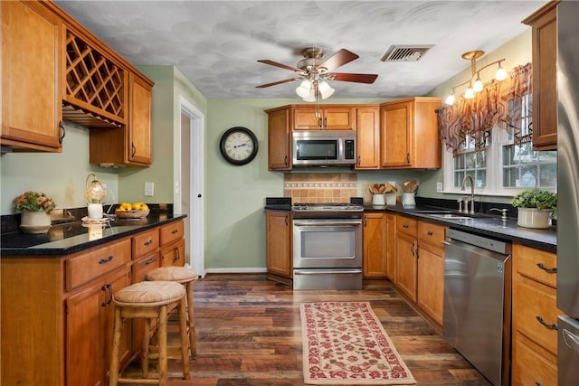 kitchen featuring ceiling fan, appliances with stainless steel finishes, a breakfast bar area, dark hardwood / wood-style floors, and sink