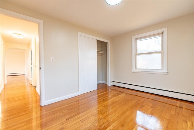 unfurnished bedroom with a closet, light wood-type flooring, and a baseboard radiator