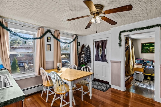 dining space featuring ceiling fan, sink, dark wood-type flooring, baseboard heating, and ornamental molding