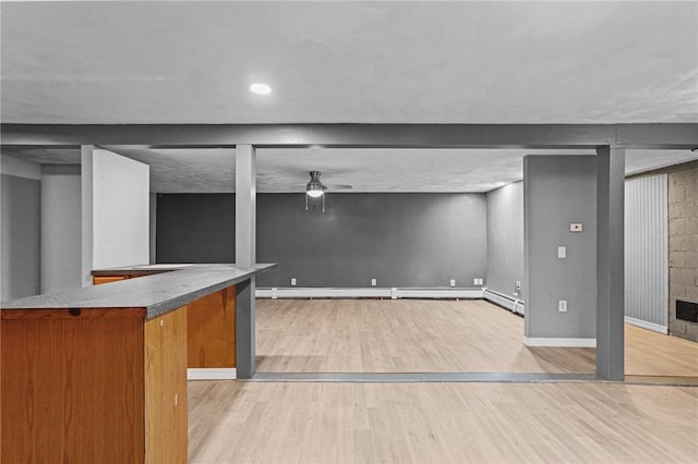 basement featuring baseboard heating, ceiling fan, and light hardwood / wood-style floors