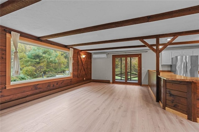 unfurnished living room featuring wooden walls, light hardwood / wood-style flooring, baseboard heating, beamed ceiling, and a wall unit AC