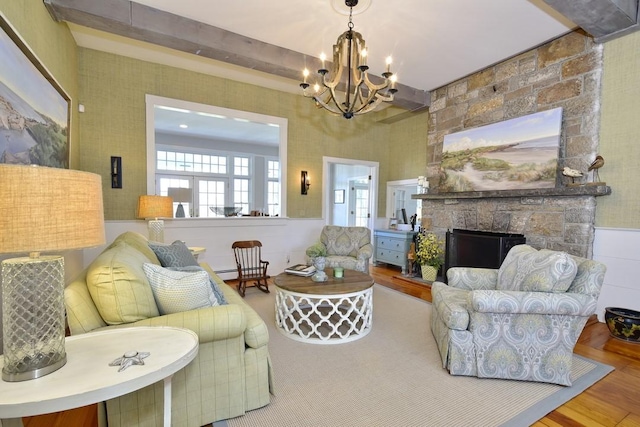 living room with beam ceiling, a stone fireplace, a notable chandelier, and wood-type flooring