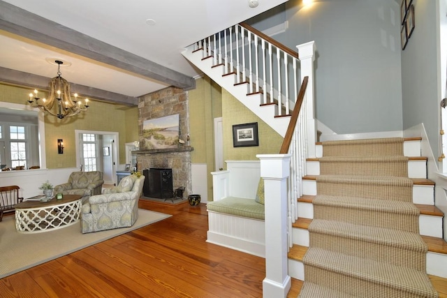 stairway featuring a stone fireplace, beamed ceiling, wood-type flooring, and an inviting chandelier