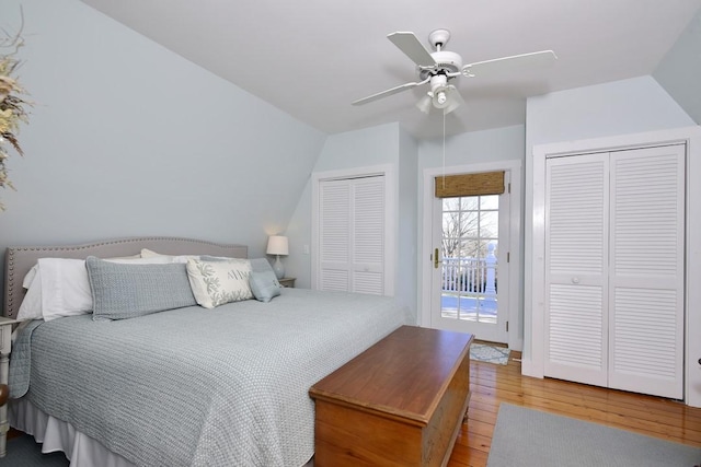 bedroom with ceiling fan, lofted ceiling, access to outside, two closets, and hardwood / wood-style flooring