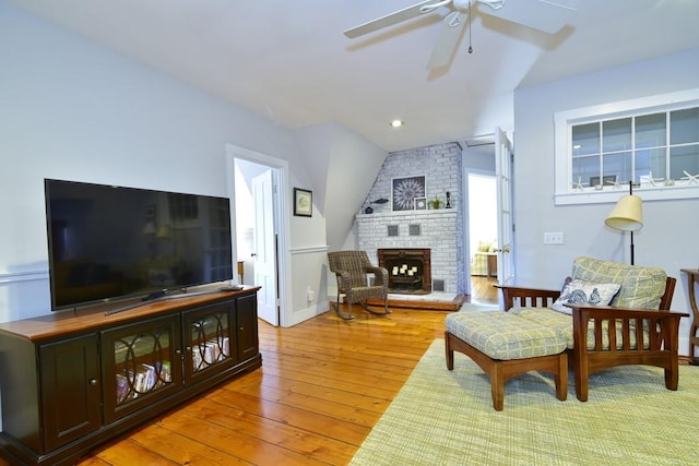 living room featuring ceiling fan, a fireplace, and light wood-type flooring