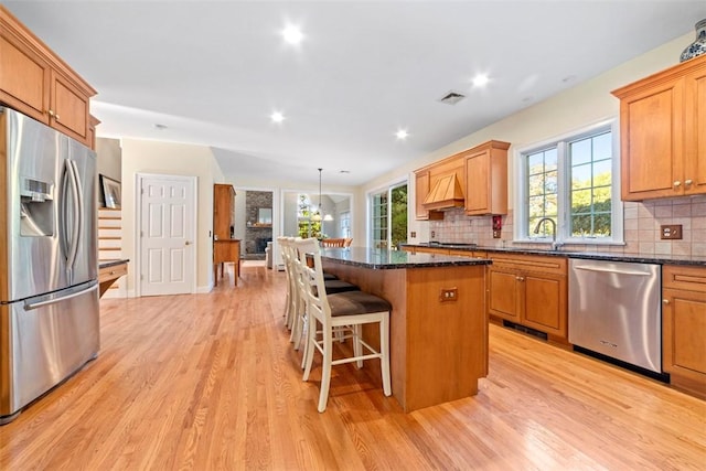 kitchen featuring a center island, hanging light fixtures, stainless steel appliances, tasteful backsplash, and light hardwood / wood-style floors