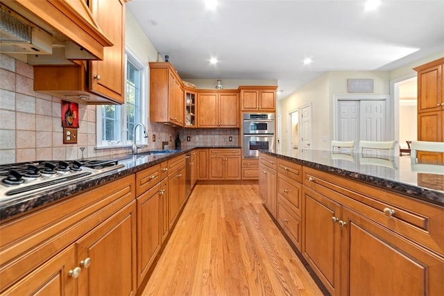 kitchen with dark stone counters, decorative backsplash, light hardwood / wood-style floors, custom range hood, and stainless steel appliances