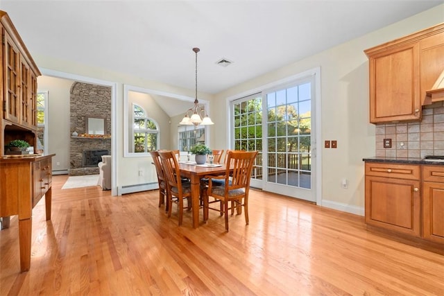 dining space featuring a baseboard heating unit, a stone fireplace, light hardwood / wood-style flooring, and vaulted ceiling