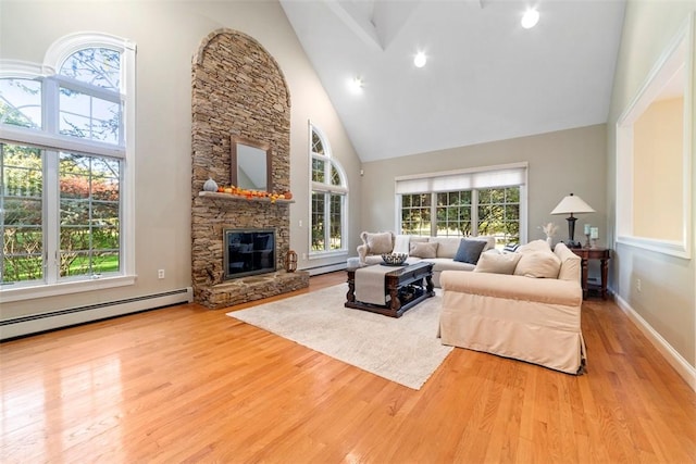 living room featuring a high ceiling, light wood-type flooring, a baseboard radiator, and a stone fireplace