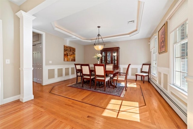 dining area featuring a raised ceiling, decorative columns, a baseboard radiator, and light wood-type flooring