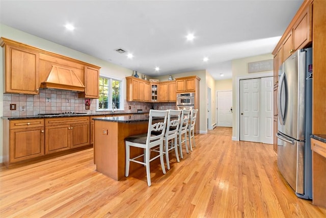 kitchen featuring appliances with stainless steel finishes, dark stone counters, light wood-type flooring, a kitchen island, and custom exhaust hood