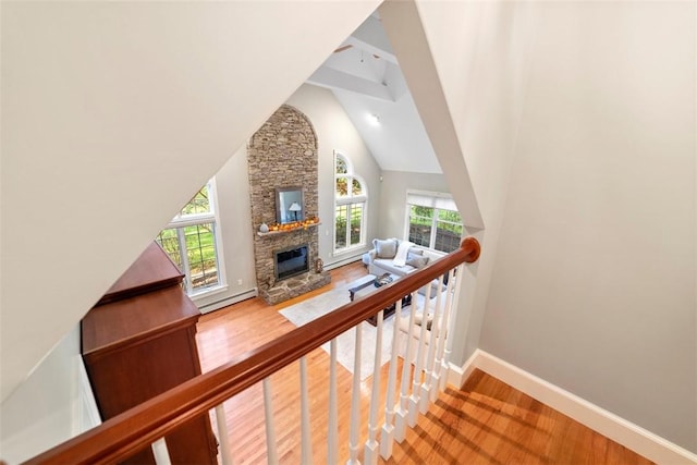 stairway with beam ceiling, high vaulted ceiling, a baseboard heating unit, a fireplace, and hardwood / wood-style flooring