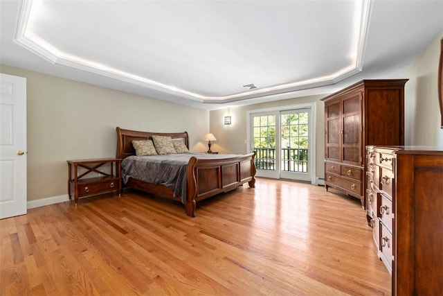 bedroom with access to outside, a tray ceiling, a baseboard heating unit, and light hardwood / wood-style floors