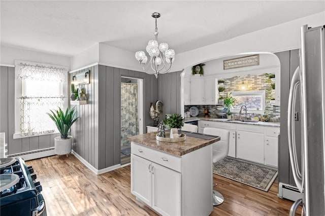 kitchen featuring white cabinetry, light wood-type flooring, stainless steel refrigerator, and decorative light fixtures