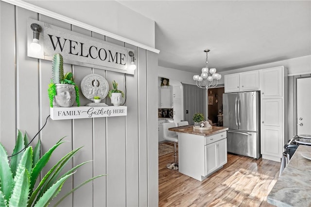 kitchen with a kitchen island, stainless steel refrigerator, white cabinets, a chandelier, and light hardwood / wood-style flooring