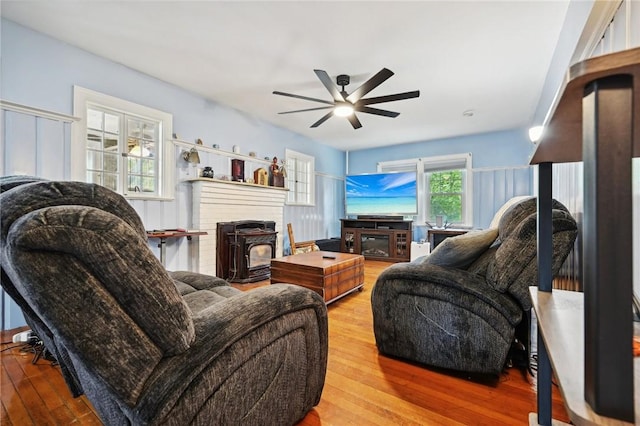 living room with a wood stove, ceiling fan, and wood-type flooring