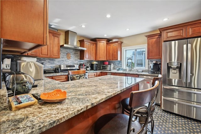 kitchen featuring light stone countertops, a breakfast bar, stainless steel appliances, and wall chimney range hood