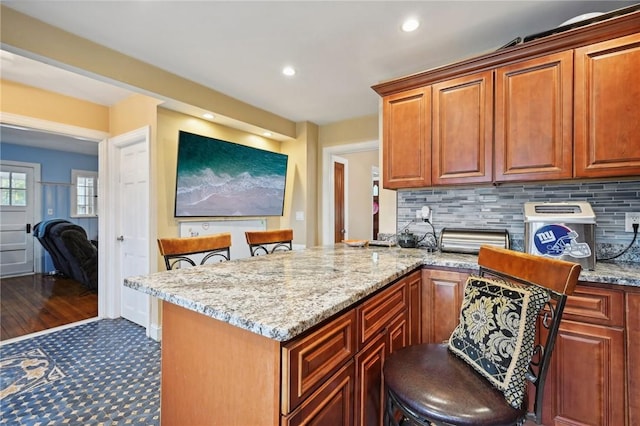 kitchen with kitchen peninsula, tasteful backsplash, light stone counters, a breakfast bar, and dark hardwood / wood-style floors