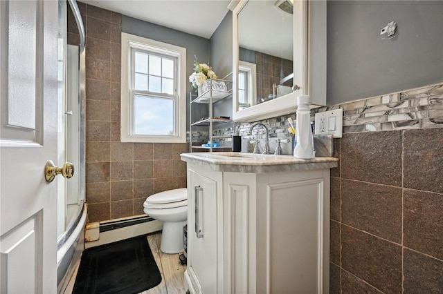 full bathroom featuring baseboard heating, combined bath / shower with glass door, toilet, vanity, and tile walls