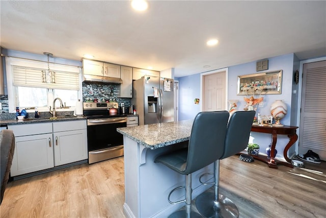 kitchen featuring appliances with stainless steel finishes, tasteful backsplash, sink, decorative light fixtures, and light hardwood / wood-style flooring