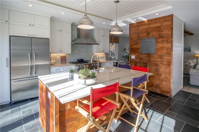 kitchen with tasteful backsplash, stainless steel built in refrigerator, pendant lighting, a center island with sink, and white cabinets