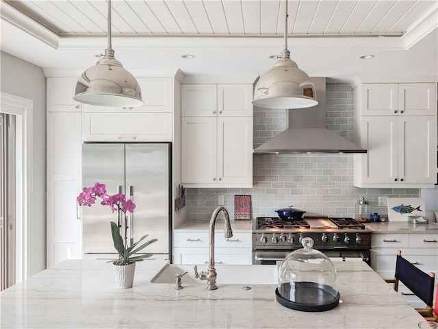 kitchen featuring light stone countertops, decorative backsplash, wall chimney range hood, decorative light fixtures, and high quality appliances