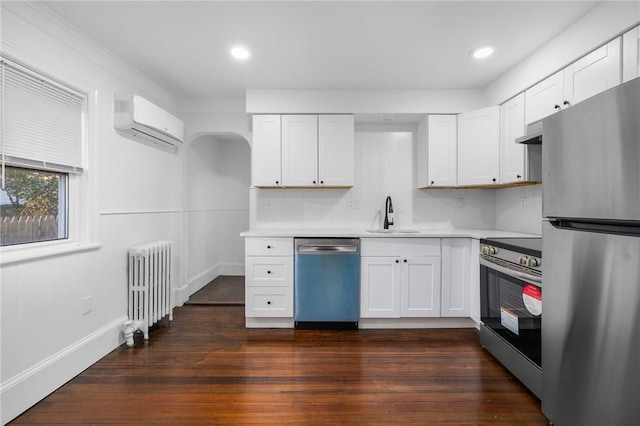 kitchen featuring radiator, sink, a wall mounted AC, white cabinetry, and stainless steel appliances