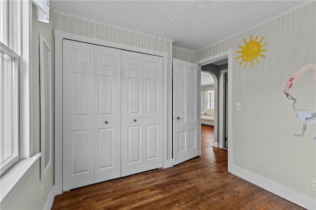 unfurnished bedroom featuring multiple windows, a closet, dark wood-type flooring, and ornamental molding