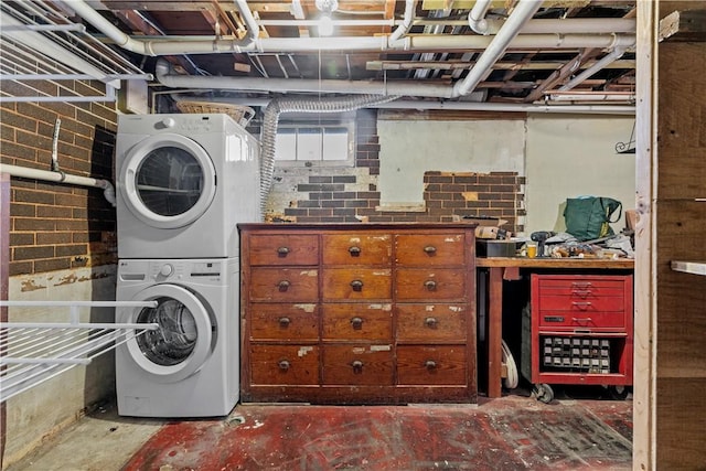 laundry area featuring stacked washer / dryer and brick wall