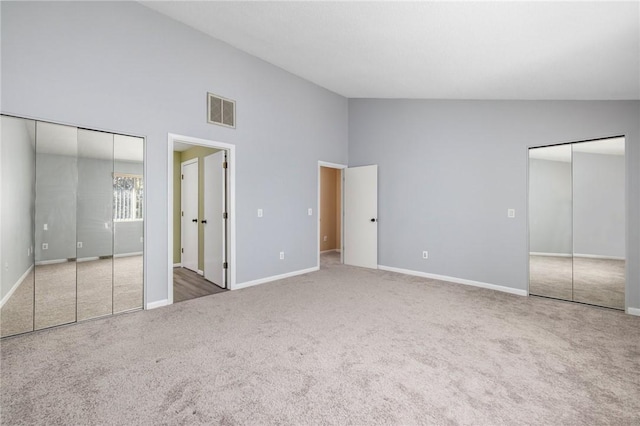 unfurnished bedroom with multiple closets, carpet floors, and high vaulted ceiling