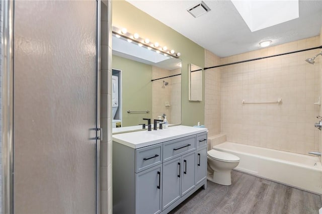 full bathroom featuring a skylight, hardwood / wood-style flooring, tiled shower / bath combo, vanity, and toilet