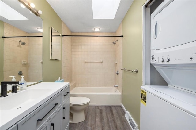 full bathroom with stacked washer / drying machine, toilet, a skylight, and wood-type flooring