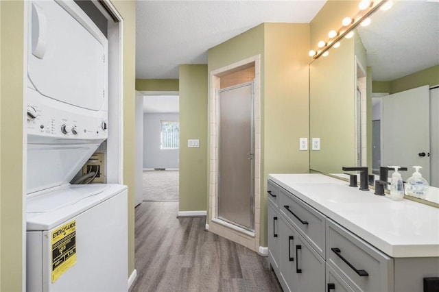 bathroom featuring stacked washer and clothes dryer, a shower with shower door, a textured ceiling, vanity, and hardwood / wood-style flooring