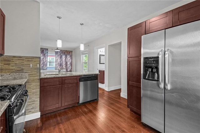 kitchen with light stone countertops, sink, dark hardwood / wood-style floors, pendant lighting, and appliances with stainless steel finishes