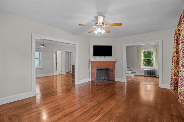 unfurnished living room featuring radiator, ceiling fan, a fireplace, and hardwood / wood-style floors