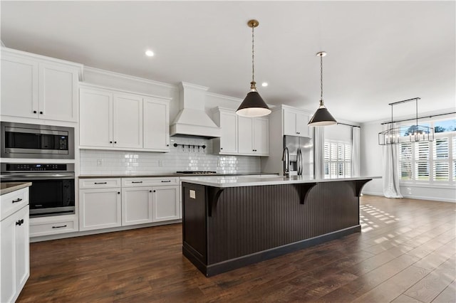 kitchen featuring premium range hood, a kitchen island with sink, a kitchen breakfast bar, decorative light fixtures, and stainless steel appliances