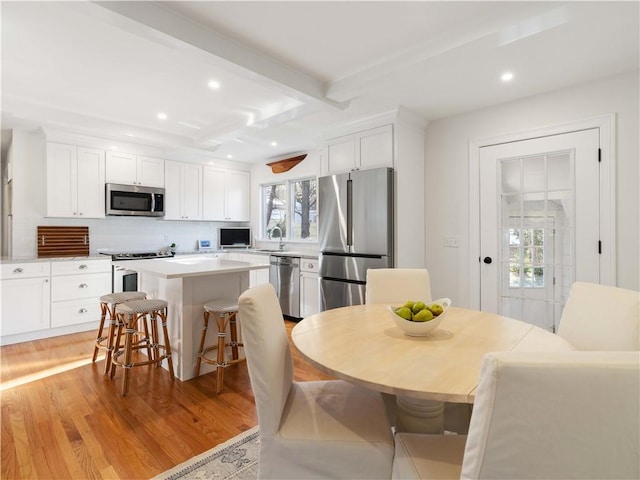 kitchen featuring beamed ceiling, a kitchen breakfast bar, stainless steel appliances, and white cabinetry