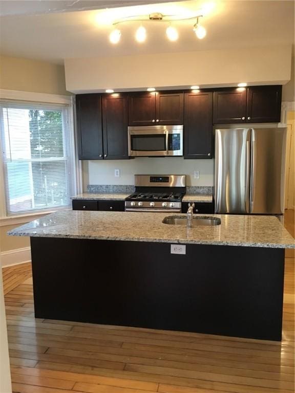 kitchen featuring light stone counters, sink, stainless steel appliances, and a kitchen island with sink