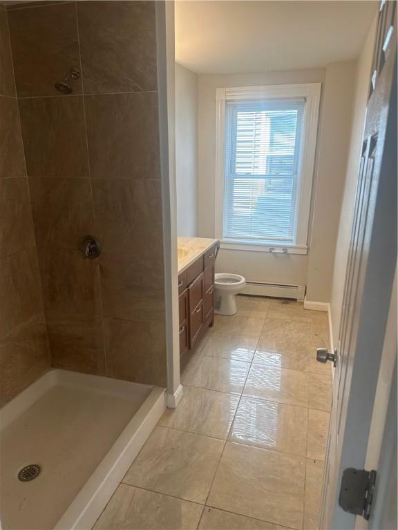 bathroom featuring a tile shower, vanity, toilet, and baseboard heating