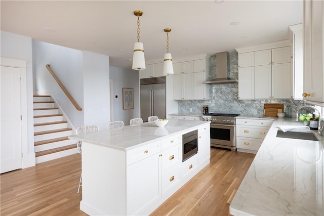 kitchen with sink, built in appliances, wall chimney exhaust hood, a kitchen island, and white cabinetry