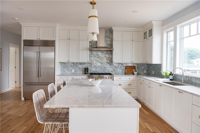 kitchen with range, wall chimney range hood, sink, decorative light fixtures, and stainless steel built in refrigerator