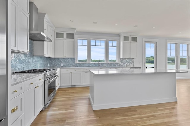 kitchen featuring high end range, wall chimney exhaust hood, light wood-type flooring, a kitchen island, and white cabinetry